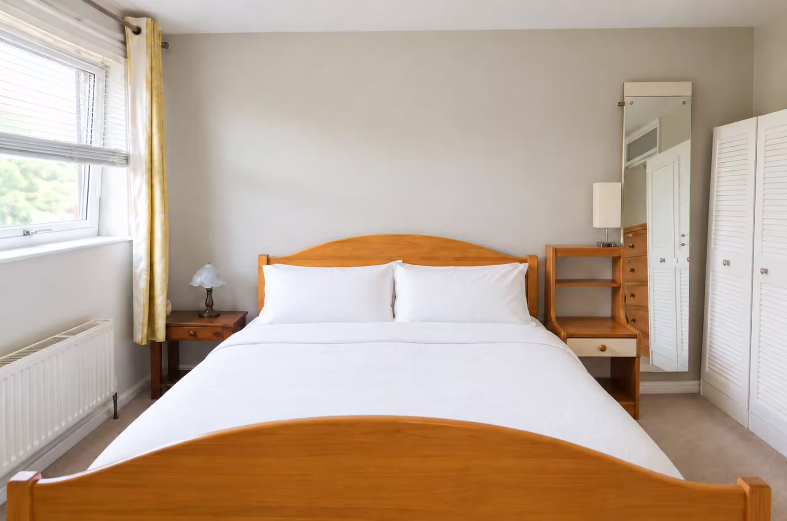 Une chambre à coucher avec un lit en bois, une table de chevet avec une lampe, une armoire et une fenêtre avec des rideaux.