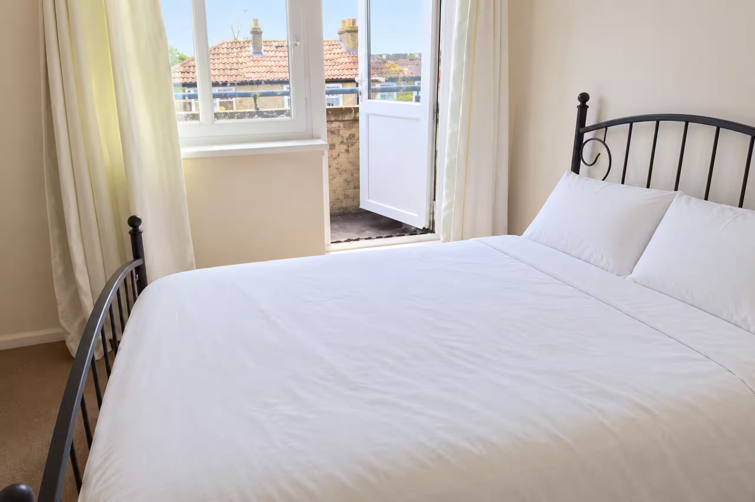A bedroom with a bed, a window, and a view of buildings outside.