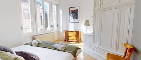 A hotel room with a bed, a wooden dresser, a chair, and a large window.