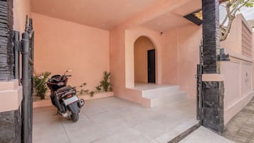 Un espace extérieur abrité où est garée une moto, un escalier menant à une porte et un petit jardin avec des plantes.