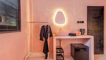 Une salle de bain comprenant un porte-serviettes, un lavabo avec un distributeur de savon, un miroir avec éclairage, un meuble noir et un espace douche.