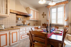 Un coin repas avec une table en bois dressée pour quatre personnes, entourée de chaises, et une cuisine en arrière-plan.