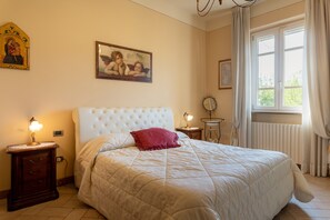 Une chambre à coucher avec un grand lit, deux tables de chevet, une commode, une fenêtre avec des rideaux et un tableau au mur.