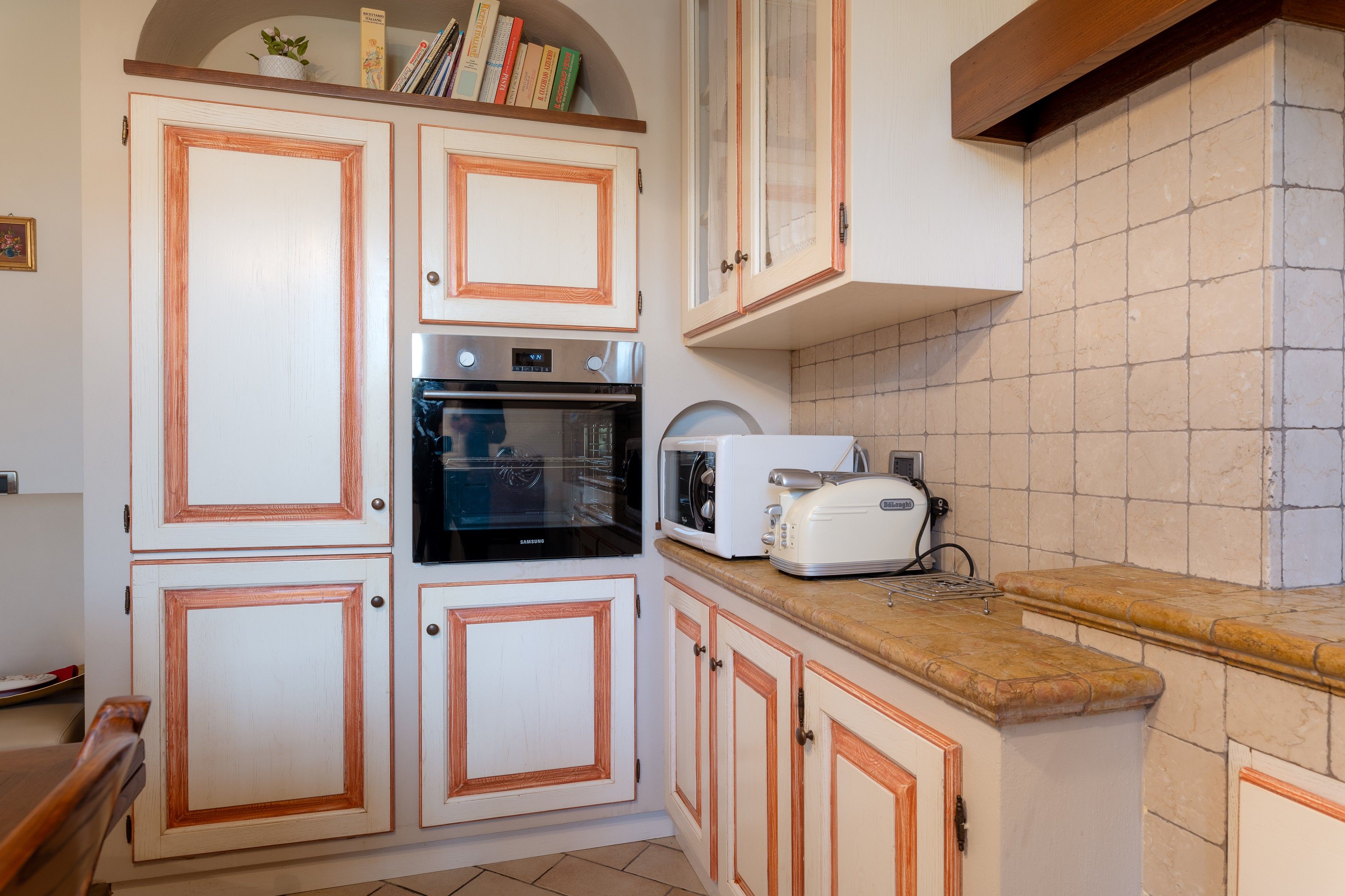 Eine Küche mit weißen Schränken, einem Backofen, einer Mikrowelle und einem Brotbackautomaten.