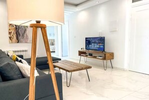 Ett modernt vardagsrum med en soffa, ett soffbord i trä, en tv på ett träställ och en tavla på väggen.