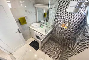A bathroom with a marble vanity, a glass shower enclosure, and a checkered tile backsplash. - The Dream House (Marsa)