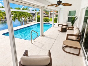 A poolside area with a view of a marina, outdoor furniture, and a ceiling fan. - Cape Coral Waterfront Retreat with Heated Pool & Dock (Cape Coral)