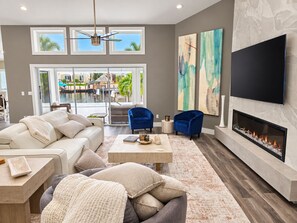 A modern living room with a fireplace, a large TV, and artwork on the wall. - Cape Coral Waterfront Retreat with Heated Pool & Dock (Cape Coral)