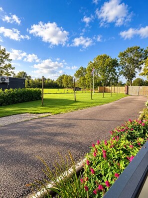 Ein gepflasterter Weg führt durch einen Park mit grünem Gras und Bäumen, einem Fahnenmast und einem Gebäude mit Klimaanlage.