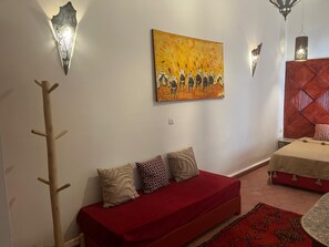 A room with a red sofa, patterned cushions, a painting, wall sconces, and a patterned rug. - Vrbo Property (Marrakech)