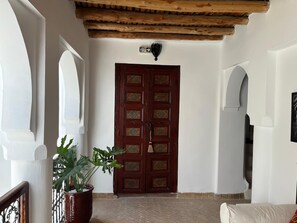 A room with a large wooden door, a potted plant, and a white wall with a small sign. - Vrbo Property (Marrakech)