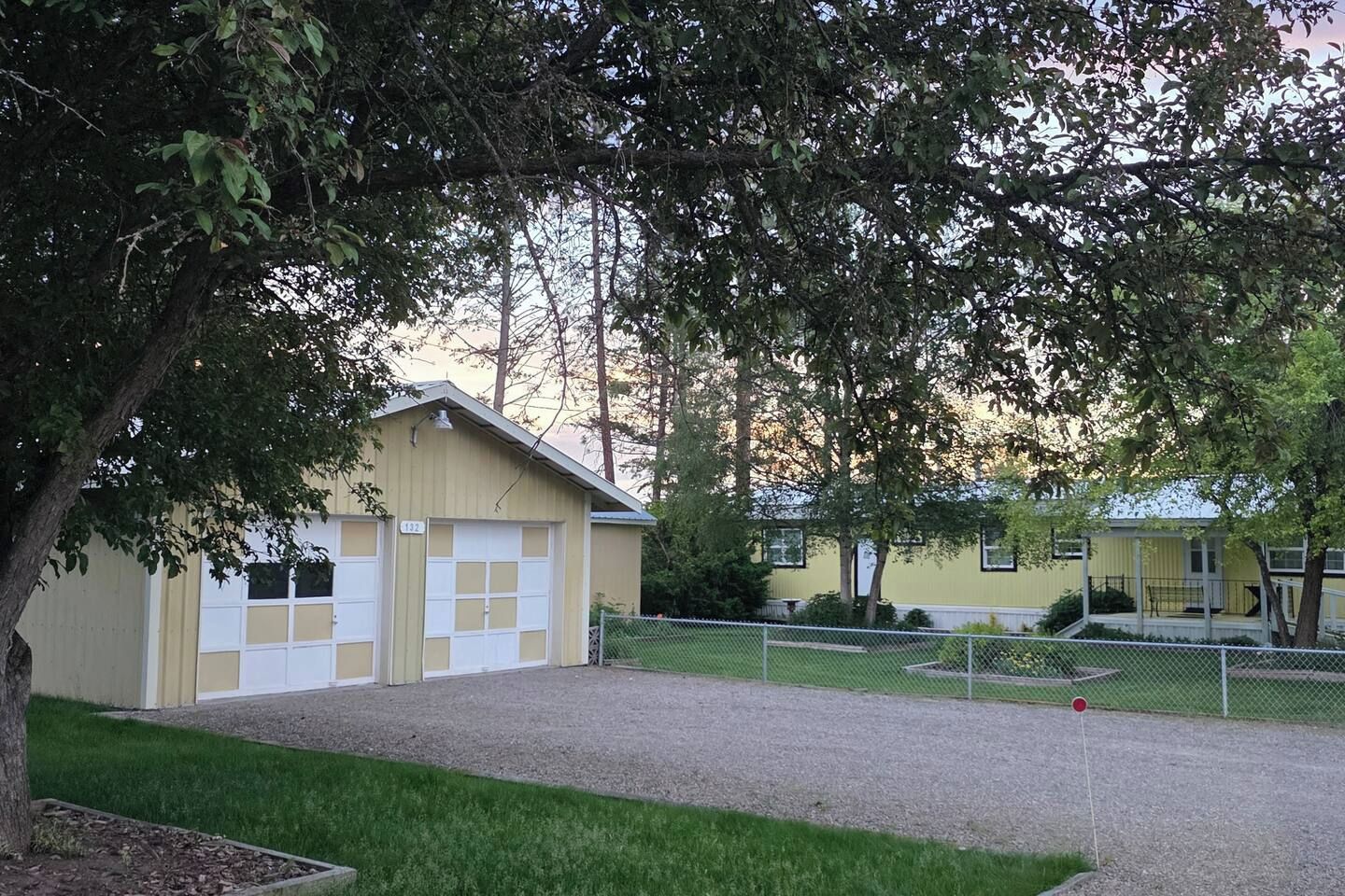 A building with a garage, surrounded by a fence and trees.