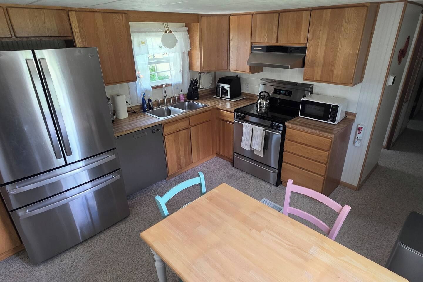A compact kitchen with a stainless steel refrigerator, a microwave, an oven, and wooden cabinets.