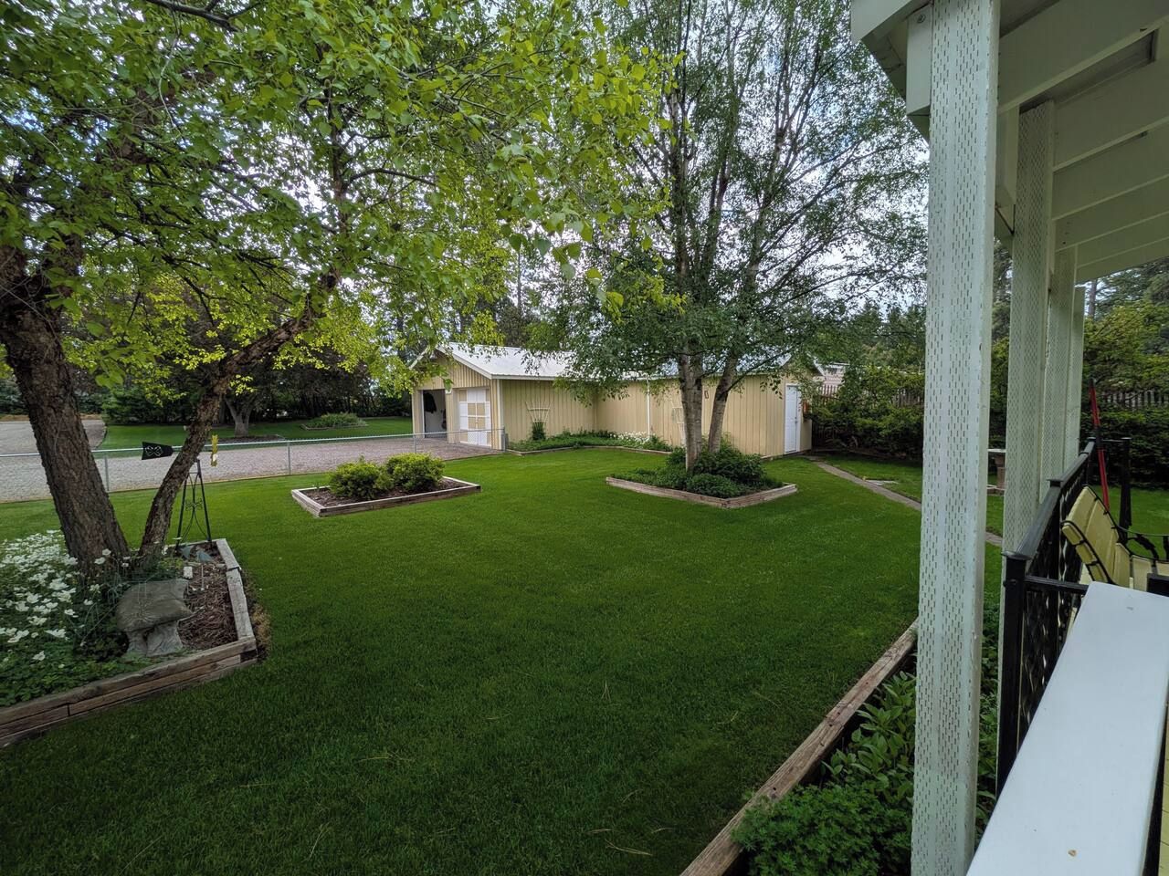 A well-maintained lawn with a house in the background, surrounded by trees and a clear sky.
