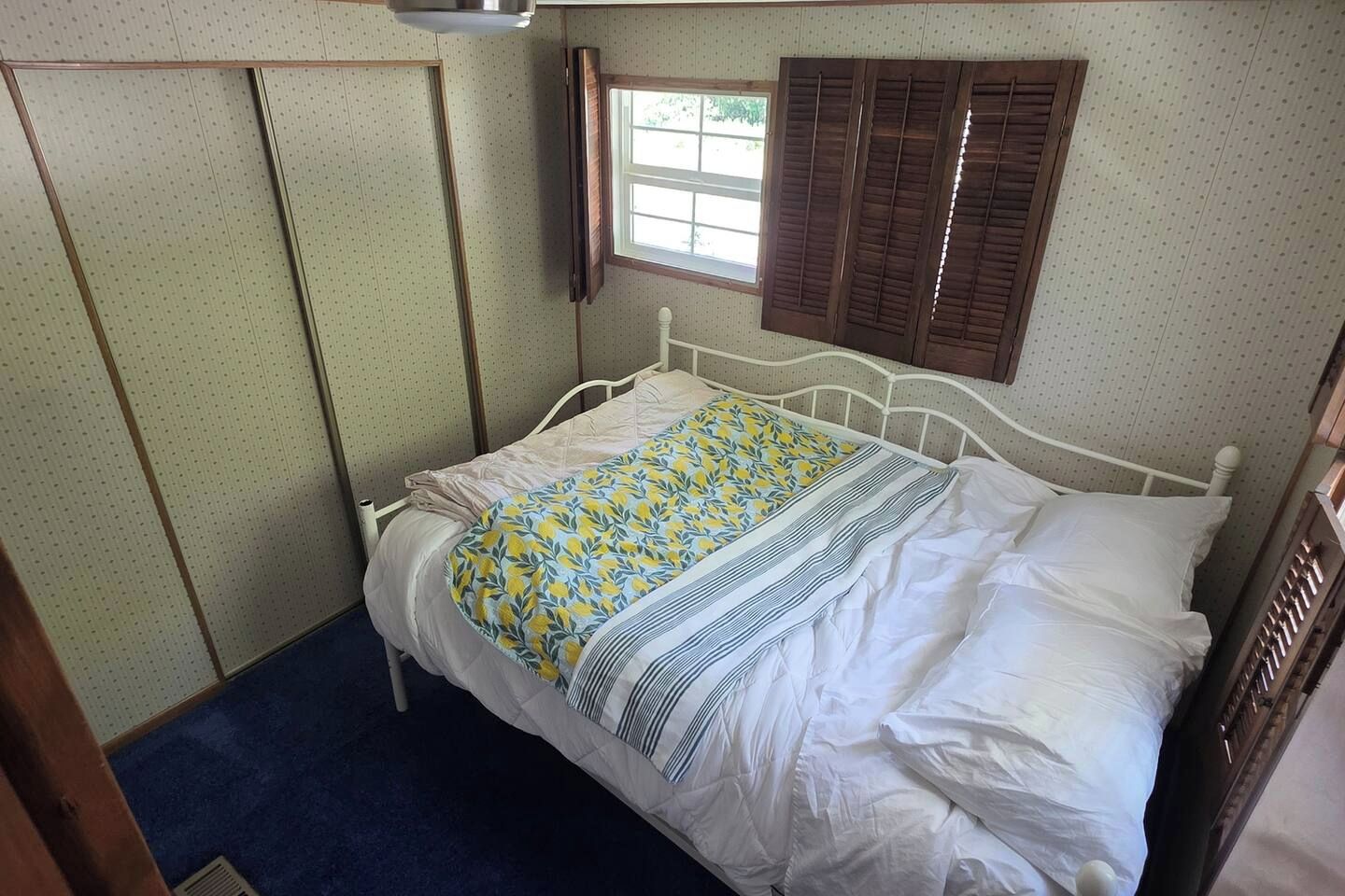 A single-bed room with a window, a wardrobe, and a bed with a patterned bedspread.