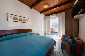 Ein Schlafzimmer mit einem großen Bett, einer Holzbalkendecke, einem gerahmten Bild an der Wand und Blick durch eine geöffnete Tür.