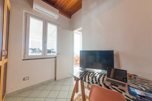 Ein Zimmer mit Glastisch, Laptop, Fernseher und einer Tür zu einem Außenbereich.