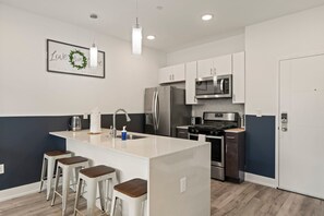 A modern kitchen with a central island, bar stools, stainless steel appliances, and a framed inspirational quote on the wall. - Urban 1BR Escape | Northern Liberties (Philadelphia)