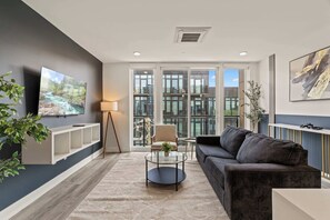 A modern living room with a sofa, a glass coffee table, a TV, and a floor lamp. - Urban 1BR Escape | Northern Liberties (Philadelphia)