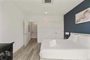 A hotel room with a bed, a desk, a chair, a door, and a wall with a painting. - Urban 1BR Escape | Northern Liberties (Philadelphia)