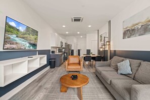 A modern living room with a sofa, a coffee table, a TV, and a kitchen area. - Modern 1BR | Sleeps 2 | Near Fishtown (Philadelphia)
