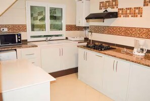 A compact kitchen with white cabinets, a microwave, a stove, and a coffee maker. - Luxury Villa with Panoramic Views (Carthage)