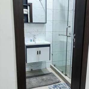 A bathroom with a glass shower enclosure, a white sink with a marble countertop, and a mirror above the sink. - 3 Bedroom Gorgeous Home, Gated with Security Cams & Mountain Views! (Oyarifa)