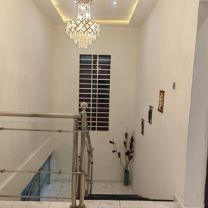 Uma escadaria com corrimão de metal, um candelabro, uma janela com persianas e um vaso com plantas.