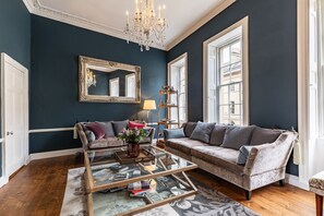 A room with a dark blue wall, a chandelier, a large mirror, two sofas, a coffee table, and a window. - Central Townhouse With Walled Garden Parking (Bath)