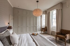 Une chambre à coucher avec un grand lit, une armoire, un coin salon avec un fauteuil et un luminaire suspendu.