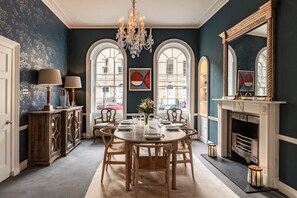 A dining room with a chandelier, a fireplace, and a view of the street through arched windows. - Central Townhouse With Walled Garden Parking (Bath)