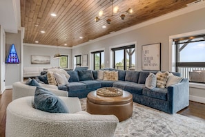 A spacious living room with a large sectional sofa, a round coffee table, and a wooden ceiling. - Mtn Views, Game Room, Fire Table, Porches (Blowing Rock)