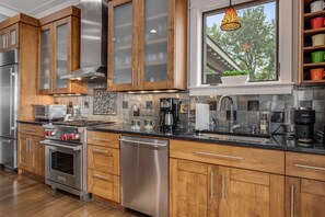 A modern kitchen with stainless steel appliances, wooden cabinets, and a window with a view of trees. - Mtn Views, Game Room, Fire Table, Porches (Blowing Rock)