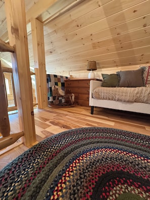 A cozy room with a wooden floor, a patterned rug, a white sofa with pillows, and a wooden dresser. - The Friendly Fern - Welcoming Old Friends and New (Old Forge)