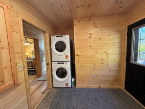 Ein Waschraum mit zwei übereinander gestapelten Waschmaschinen, Holzvertäfelung und einer Tür zu einem Badezimmer.