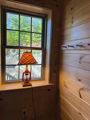 Ein Fenster mit einer Lampe auf der Fensterbank, Holzpaneele an der Wand und Blick auf Bäume draußen.