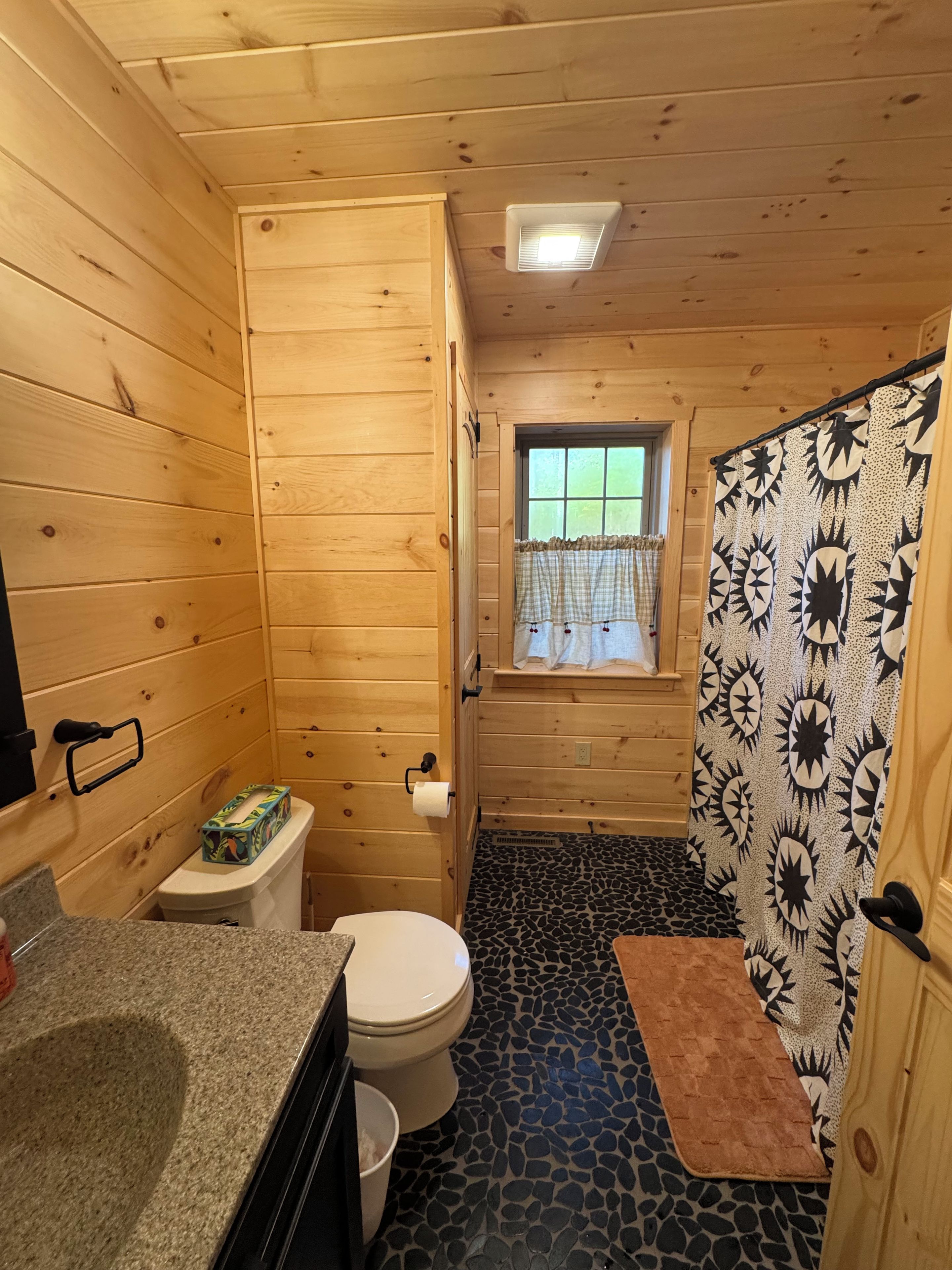 Une salle de bain rustique, aménagée dans une cabane en bois, avec des toilettes, un lavabo et une fenêtre.