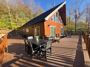 A log cabin with a deck, outdoor seating, and a view of the surrounding forest. - The Friendly Fern - Welcoming Old Friends and New (Old Forge)