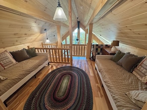 A cozy cabin interior with two wooden beds, a woven rug, and a wooden railing. - The Friendly Fern - Welcoming Old Friends and New (Old Forge)