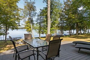En terrasse med et bord og stole med glasplade, der kigger ud over en sø med både og træer.
