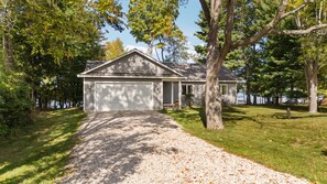 A single-story house with a garage, surrounded by trees and a gravel driveway. - Sleeping Bear Dunes Lakefront Getaway (Empire)