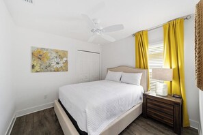 Ein Schlafzimmer mit einem Bett, einem Nachttisch, einem Deckenventilator, einer Tür und einem Fenster mit gelben Vorhängen.