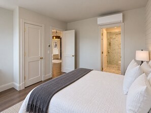 Un dormitorio con cama, lámpara de noche y baño visible a través de una puerta abierta.