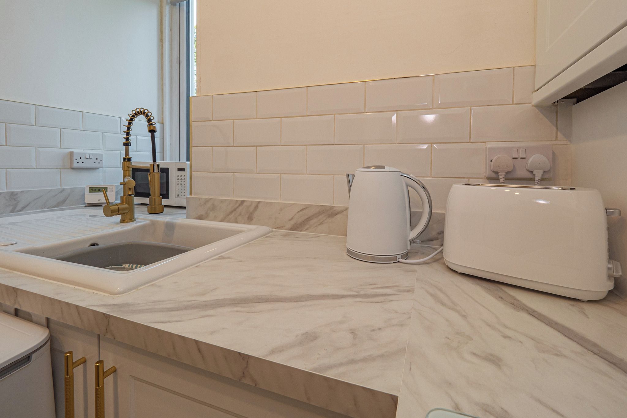 Een moderne keuken met een spoelbak, waterkoker en broodrooster op het aanrecht.
