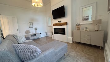 Ein modernes Schlafzimmer mit einem großen Bett, einem flachbildfernseher über einem Kamin und einer Kommode mit Schubladen.