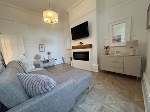 Ein modernes Schlafzimmer mit einem großen Bett, einem flachbildfernseher über einem Kamin und einer Kommode mit Schubladen.