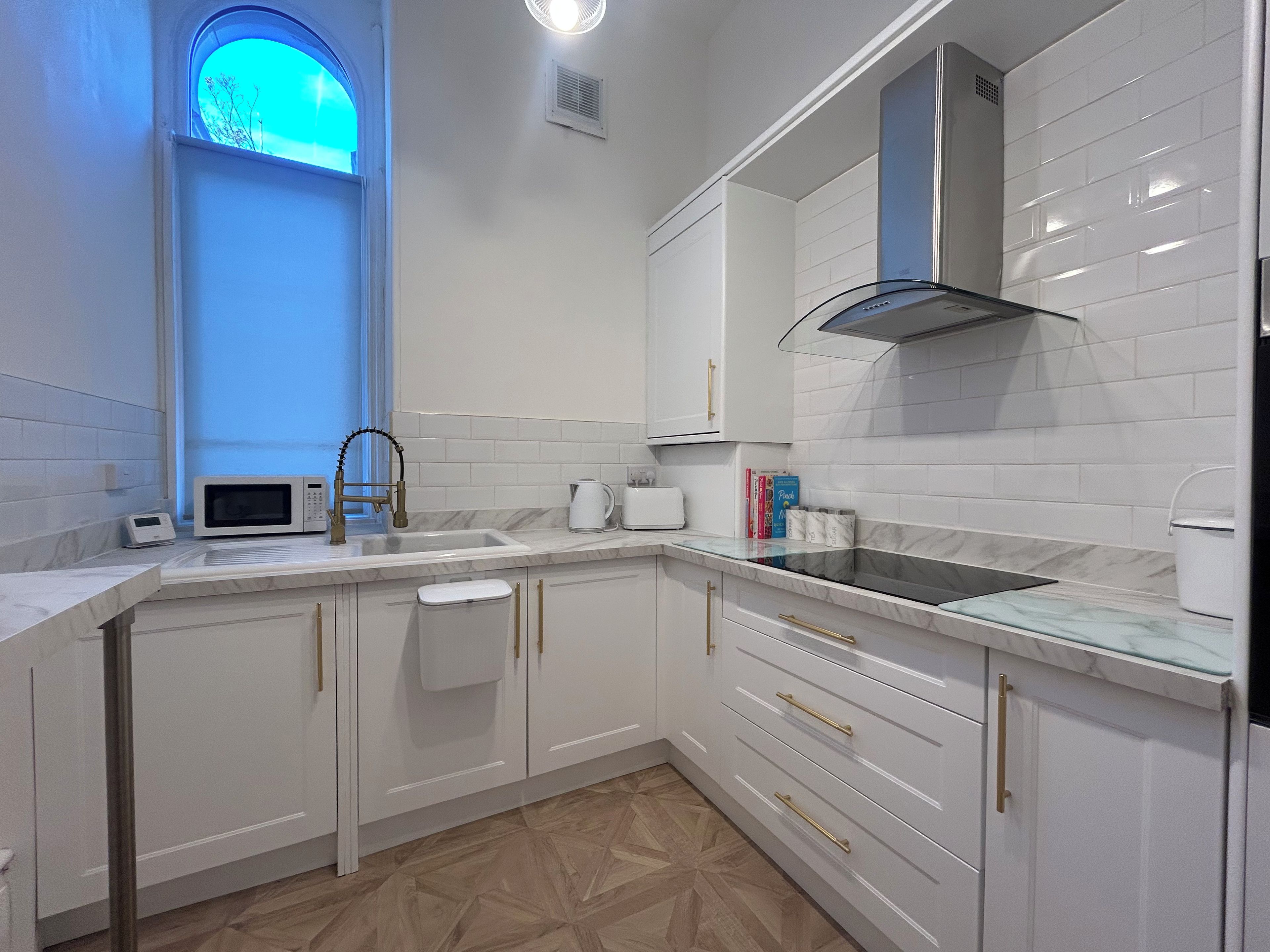 A modern kitchen with white cabinetry, a stainless steel sink, and a window with a blue tint.