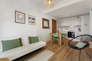 A modern living room with a white sofa, green cushions, a dining table with chairs, and a kitchen area with white cabinets and appliances. - Apartment 'Salsedine's House' with Private Garden, Wi-Fi and Air Conditioning (Arboriamar)