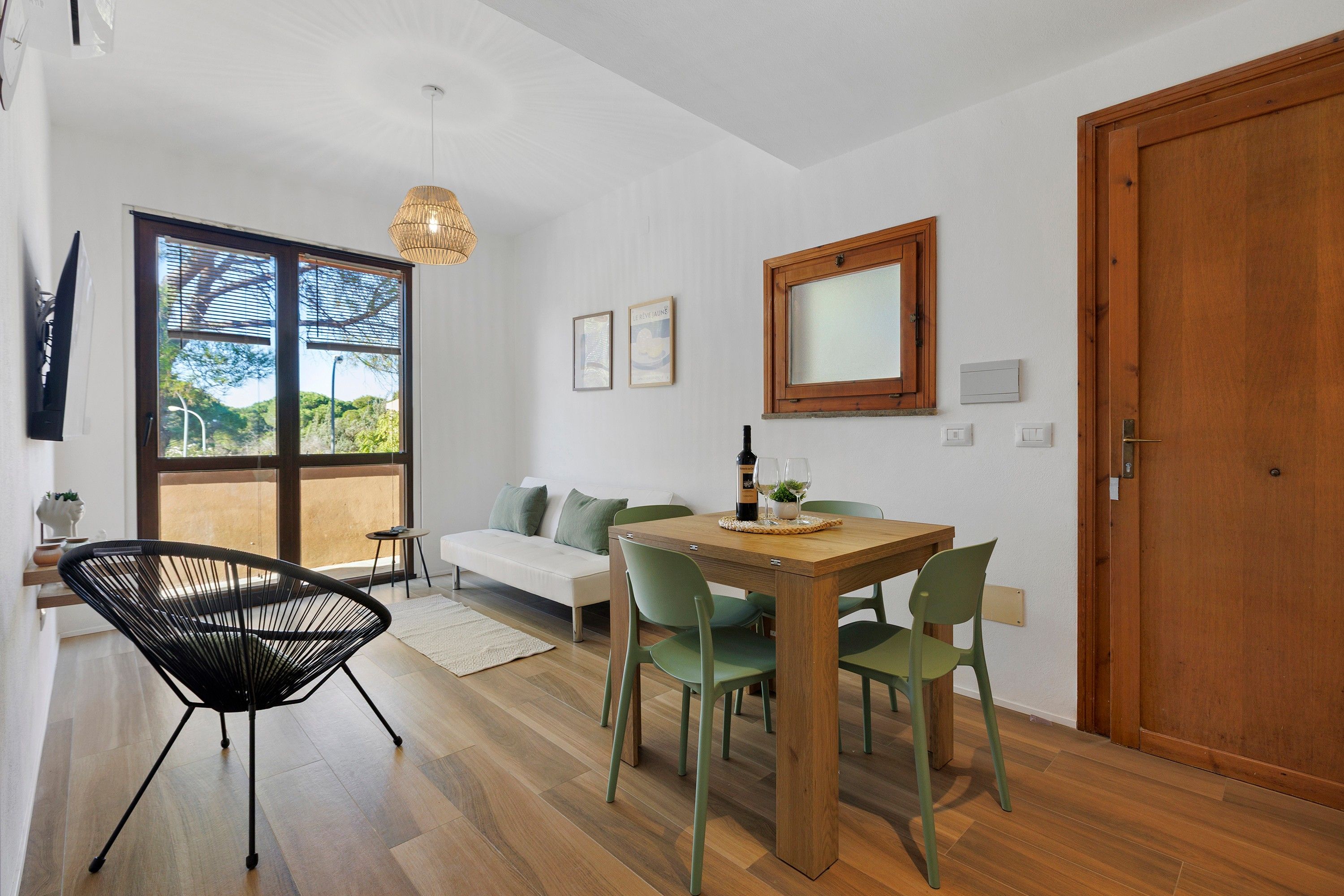 A modern living space with a dining area, a sofa, a wooden table, and a large window offering a view of greenery.