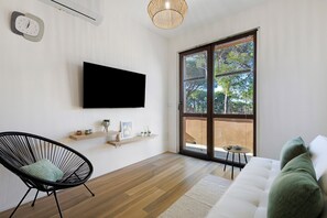 A modern living room with a flat-screen TV, a wicker chair, a white sofa, and a large sliding glass door leading to an outdoor area. - Apartment 'Salsedine's House' with Private Garden, Wi-Fi and Air Conditioning (Arboriamar)